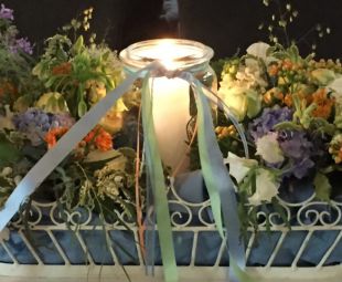 Hochzeits-Tischgesteck: Vintagekorb mit Windlicht und passenden Baendern ummantelt von pastell-farbenen Blumen
