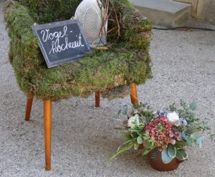 Hochzeitsgaeste Willkommens Deko: Sessel mit Moosmantel, Vogelkaefig mit Baenderdeko, Hinweisschild und romantischer Blumenstrauss in Tontopf