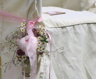 Freie Trauung: Stuhl mit weißer Husse, mit rose Schleifenband umlegt, mit mini Blumensträußchen Pfingstrose, Kamille, rose Schleierkraut in Glasfläschchen, DIY-Tüte mit Tuch für Freudenstränen