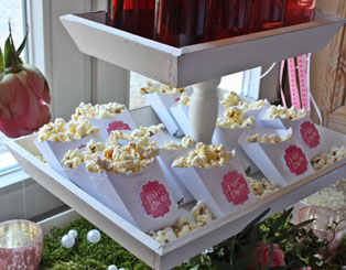 Willkommen-Station für Gäste Event: Weiße Holzetagere, kleine Schachteln mit Textbutton "Für Dich" mit Popcorn gefüllt, Event Dekoration Rosenköpfe von der Decke hängend, rosé Teelichter auf Moosbett, Blumenstrauß und Perlen